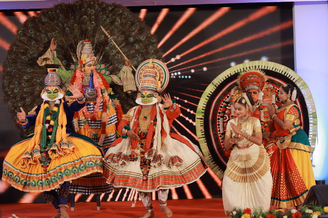 Kathakali performers in towering headdresses and bright costumes on a lit stage
