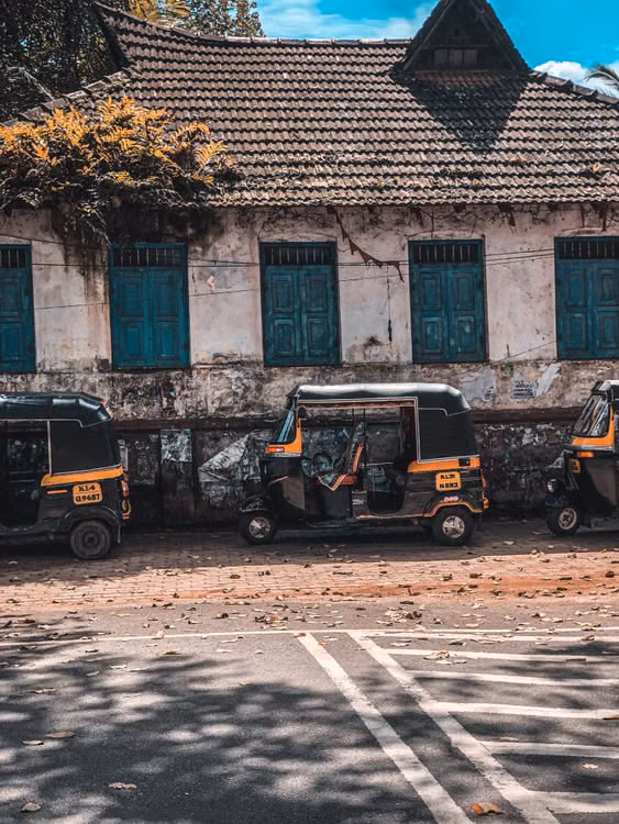 Auto-rickshaws parked before a weathered colonial building with green shutters and a tiled roof