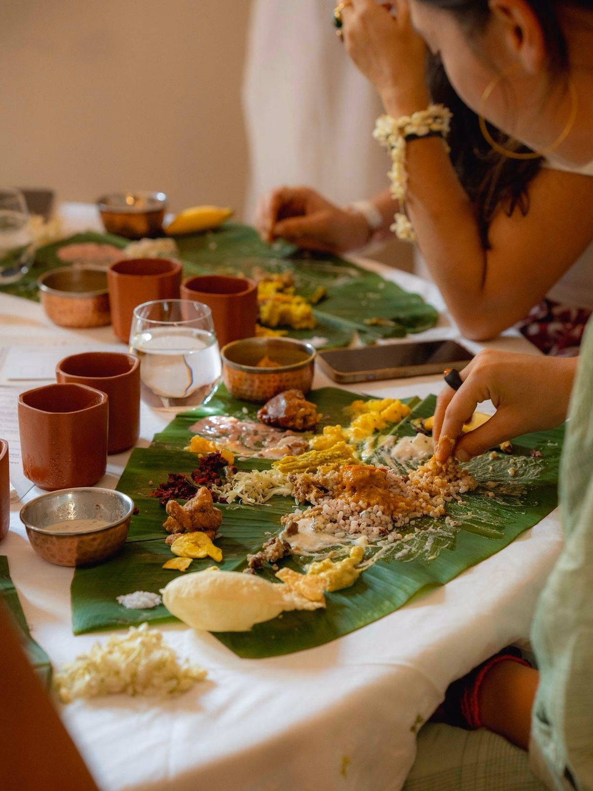 A shared meal served on banana leaves, small bowls of curries and rice laid out along the table