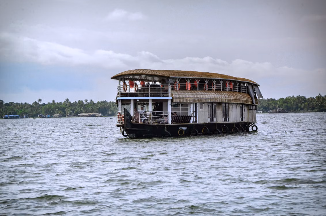 A houseboat moving across open backwater, a green shoreline behind it