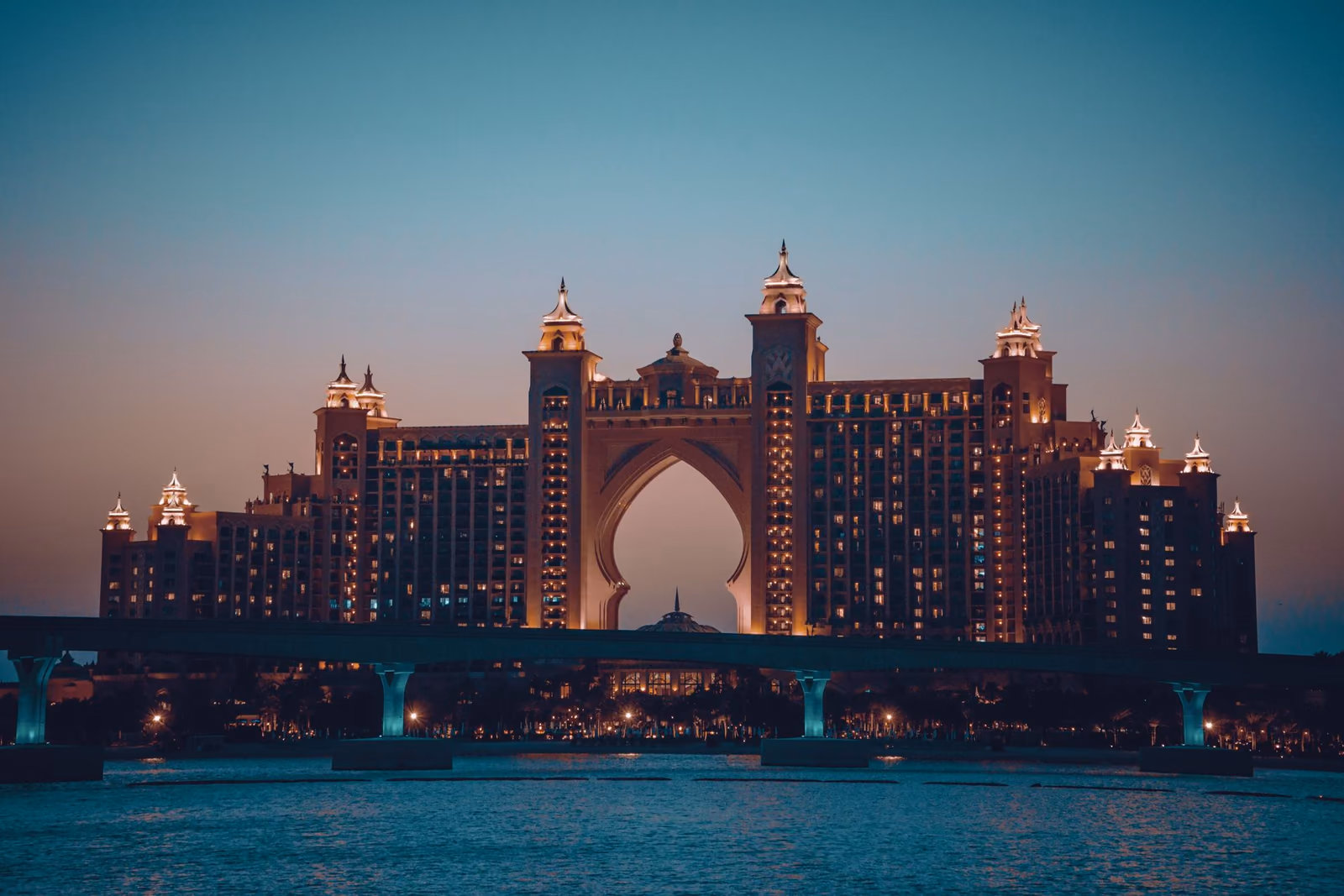 A grand arched resort glowing against the dusk sky across the water