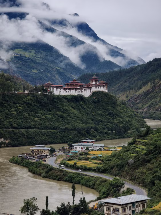 A white fortress above a river valley beneath mountain cloud