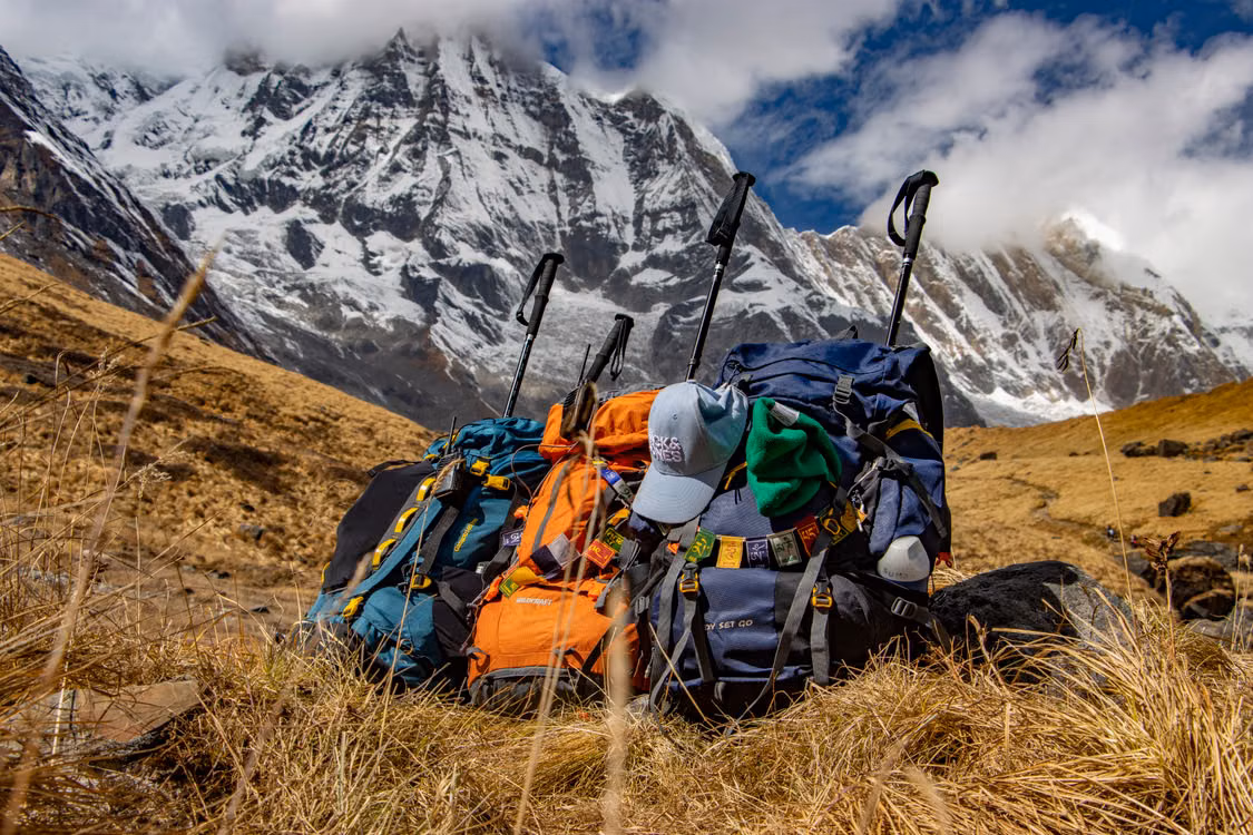 Trekking packs and poles in a mountain meadow below snow peaks