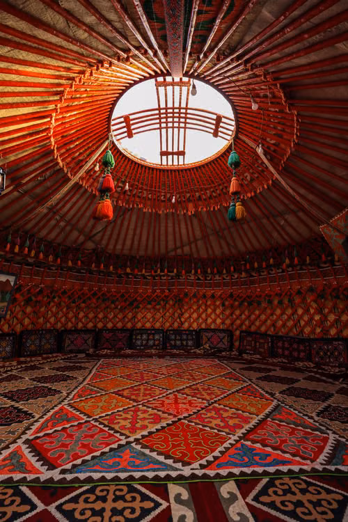 The red patterned dome of a yurt above a woven carpet