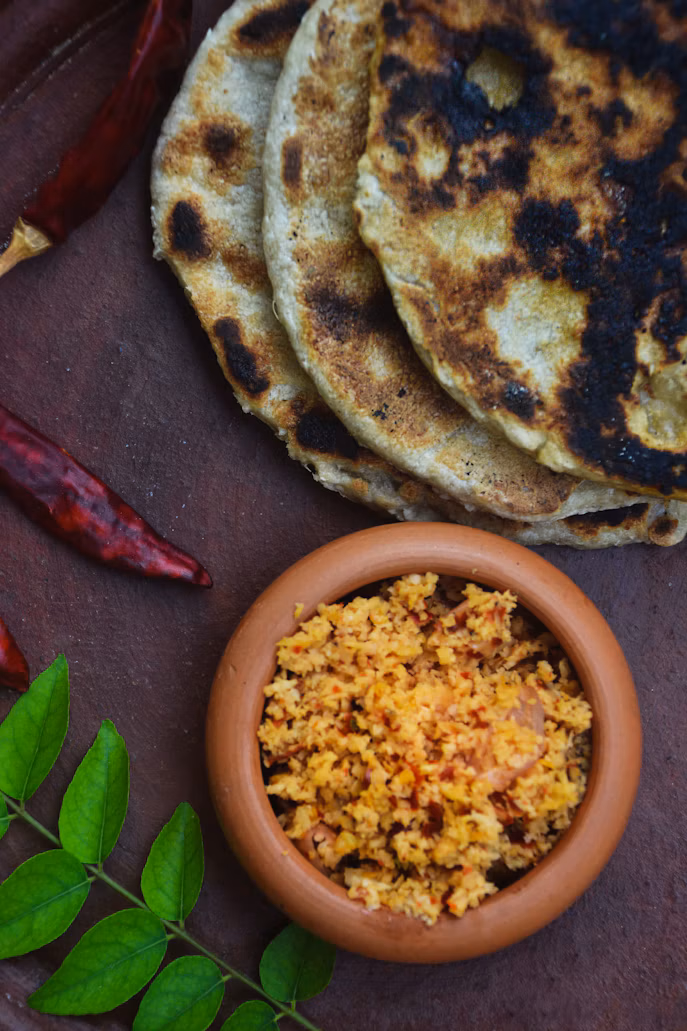 Flatbreads and a clay bowl of spiced coconut beside curry leaves