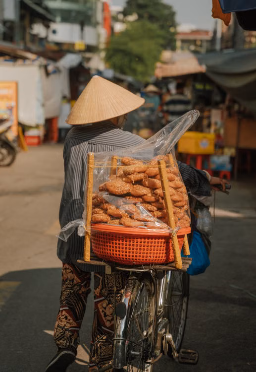 A vendor in a conical hat carrying baskets on a bicycle