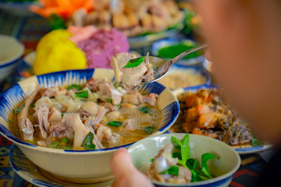 A hand serving bowls of noodle soup among plates of food
