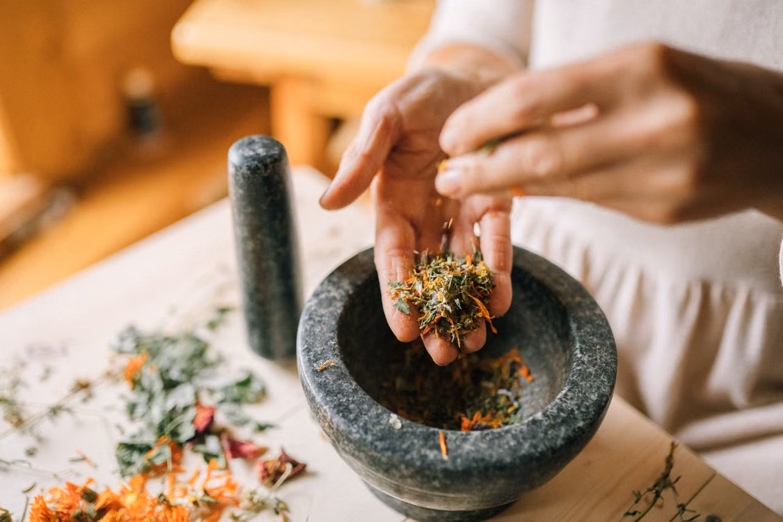 Hands crushing herbs in a stone mortar