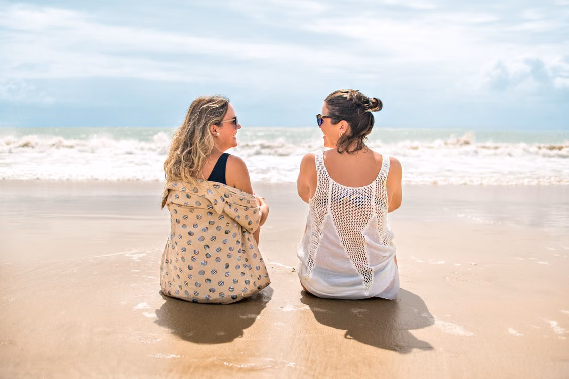 Two women sitting together on a beach, looking out to sea