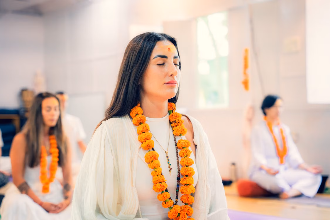 A woman in a marigold garland meditating in a yoga class