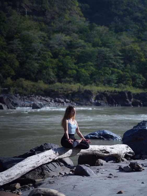 A woman sitting on a driftwood log beside the river