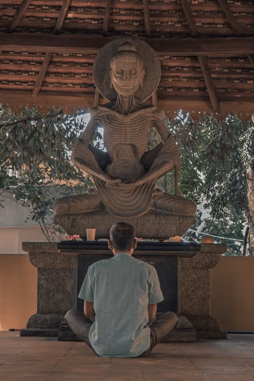 A man seated in front of a stone meditation statue