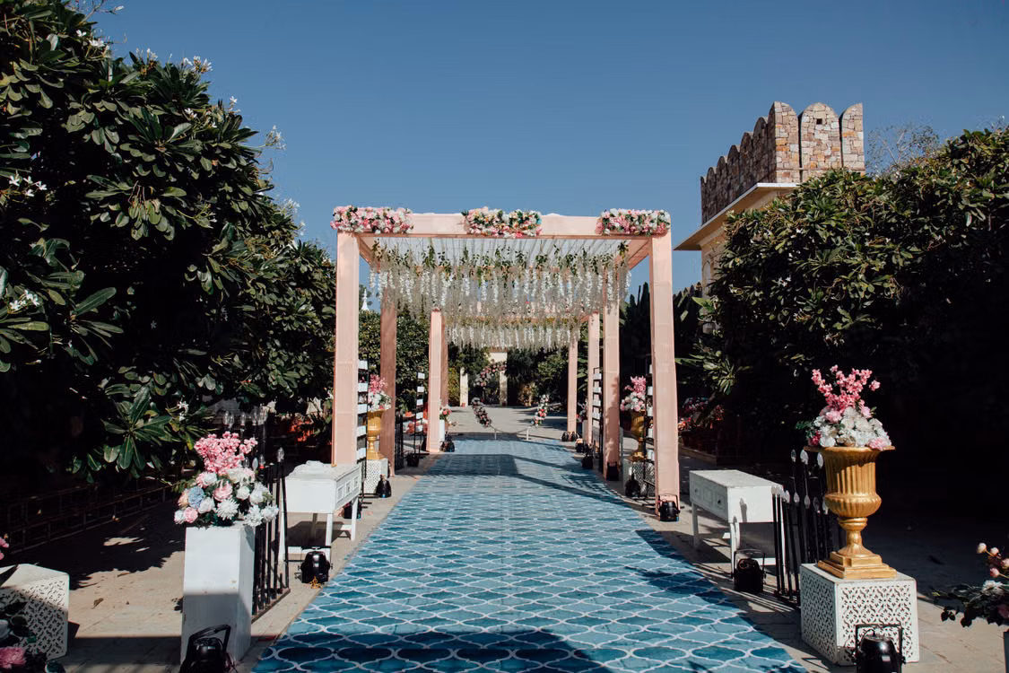 A pink floral mandap at the end of a tiled aisle, with the fort wall behind, Jodhpur