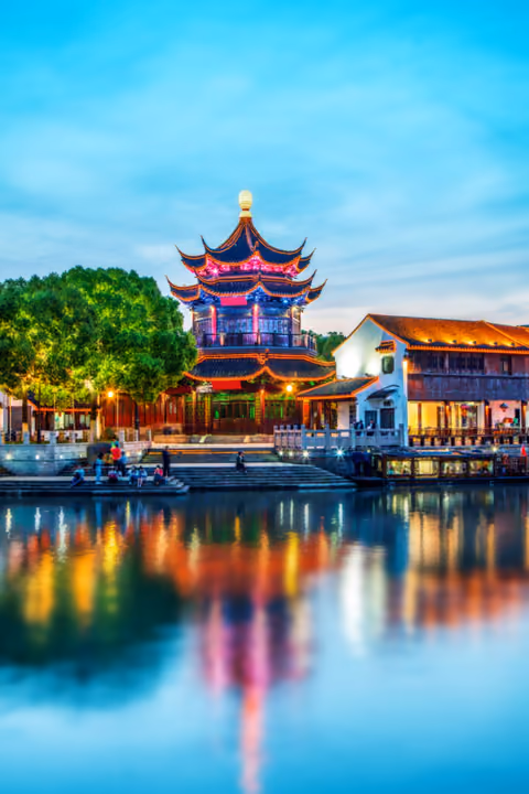 A lantern-lit pagoda glowing over a canal at dusk