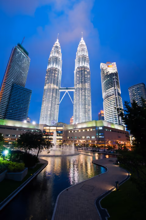 The illuminated Petronas Towers reflected in a fountain-lit plaza