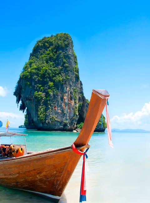 A traditional longtail boat below a limestone karst on a turquoise bay