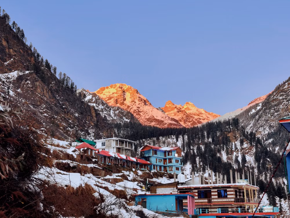 Manali's snowy rooftops below peaks glowing at sunset