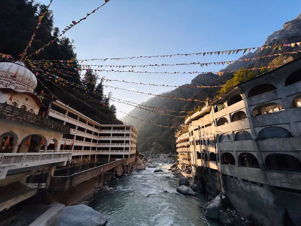 Gurudwara buildings above the river, with prayer flags overhead