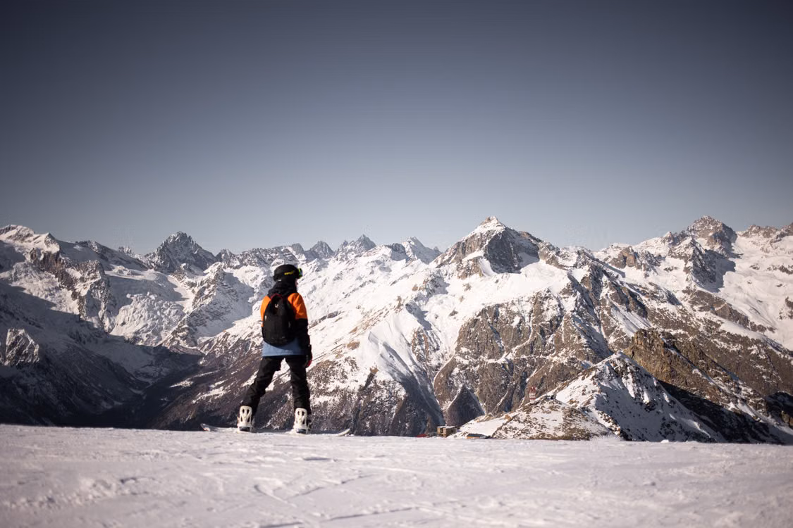 A skier standing on a snowfield facing jagged peaks
