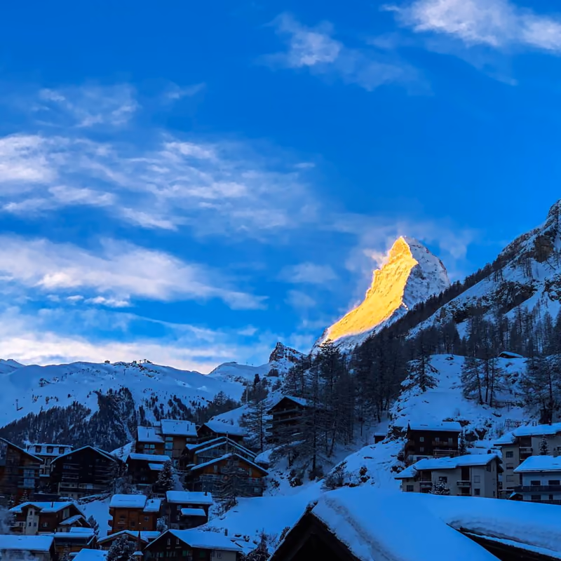 Snow-dusted chalets below an alpine peak lit gold at dusk