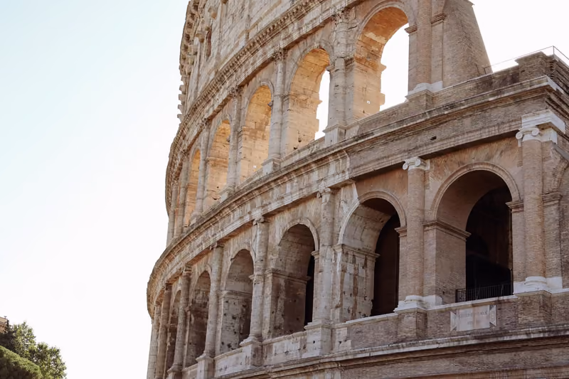 The weathered stone arches of the Colosseum in Rome against a pale sky