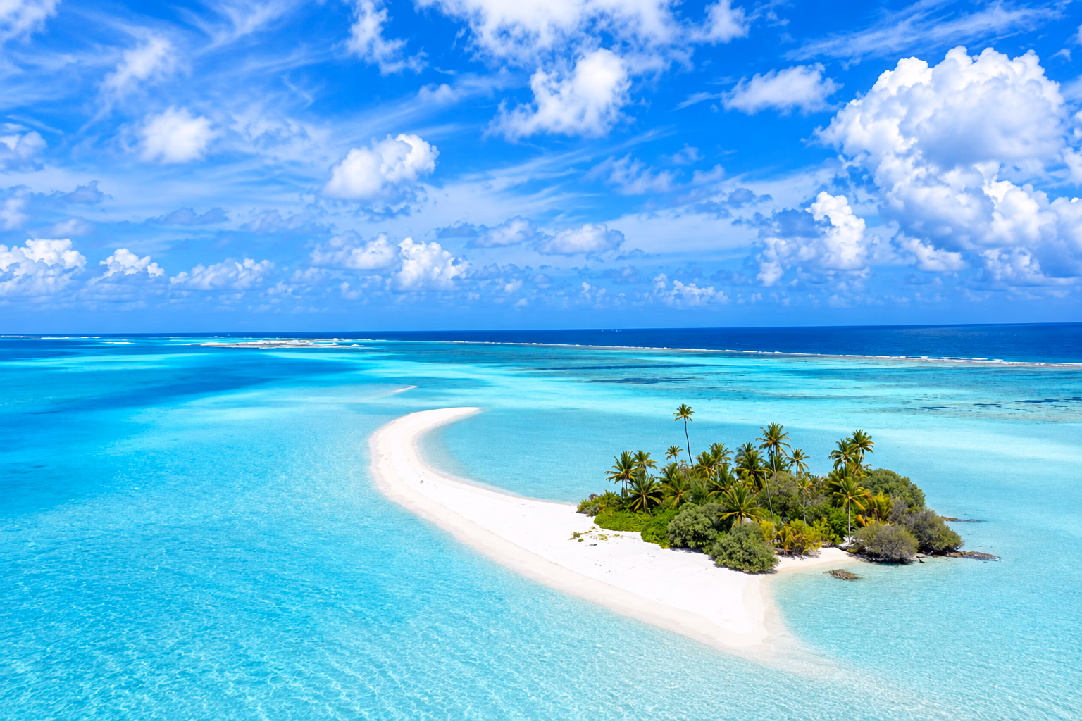 A palm-covered sandbar island ringed by turquoise lagoon water