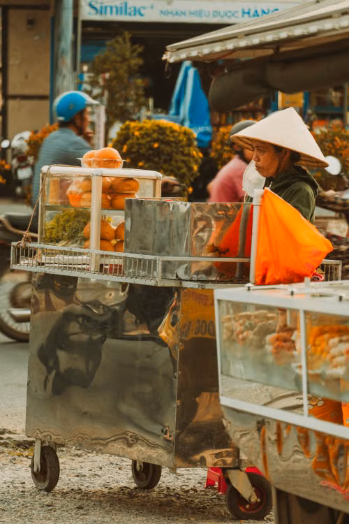 A street vendor in a conical hat beside a loaded cart
