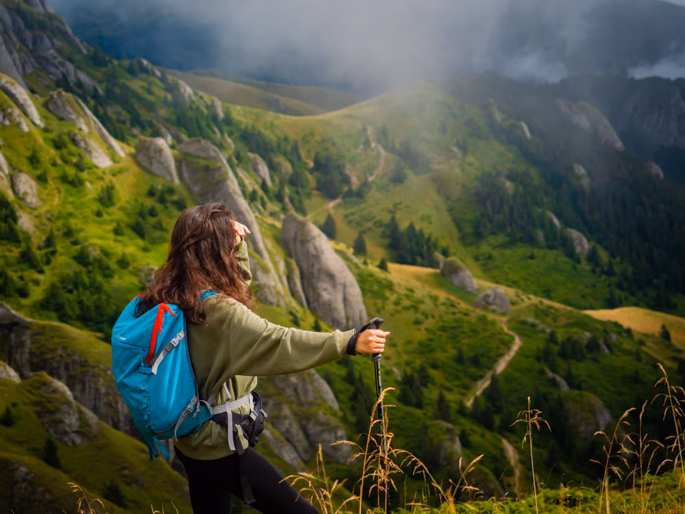 A hiker with a teal backpack on a green mountain ridge