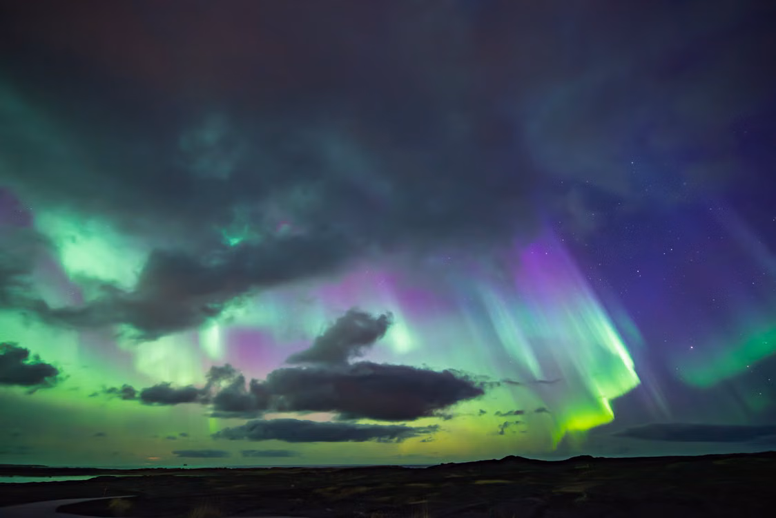 Green and purple northern lights above a dark horizon