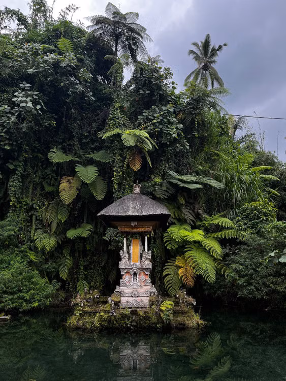A small stone shrine beside a pond in lush tropical forest