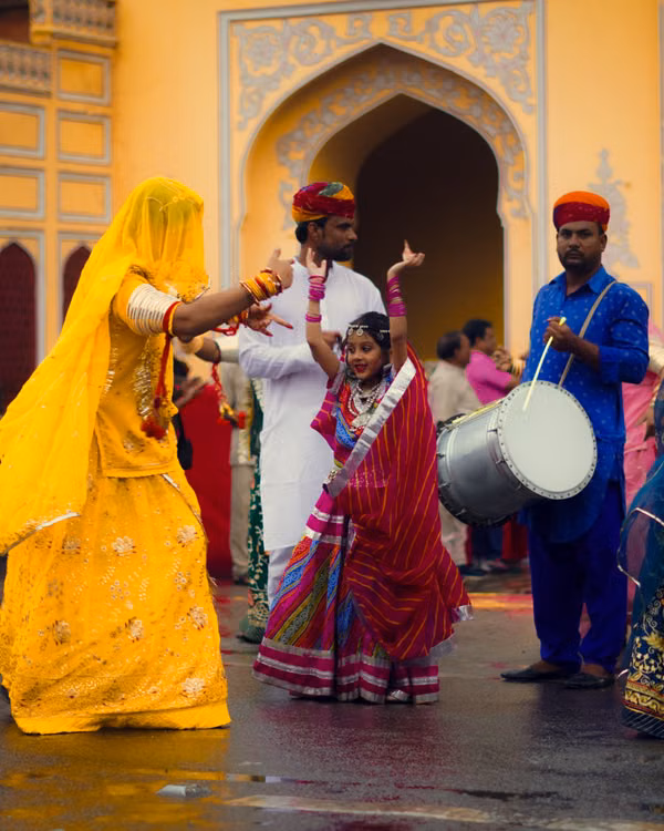 Dancers in bright yellow and red costumes beside a drummer in front of an arched doorway