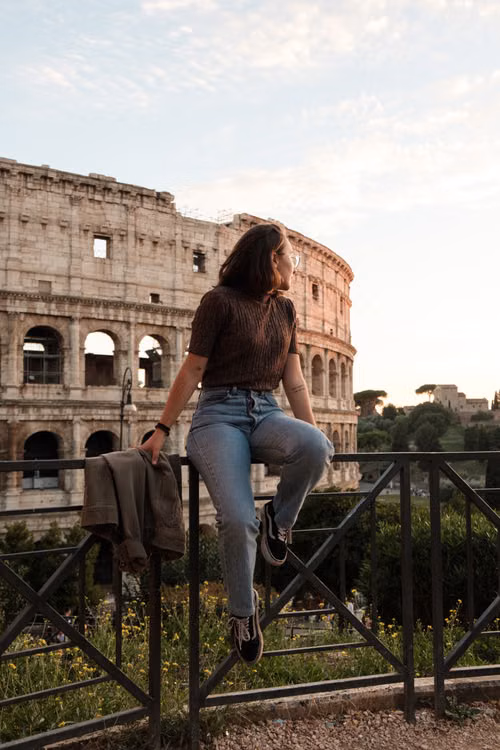 A woman sitting on a railing in front of the Colosseum at sunset