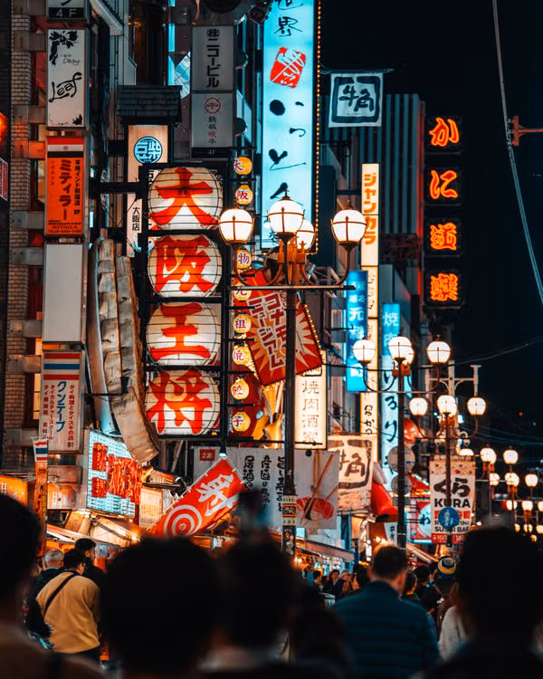 A crowded street at night under glowing neon signs