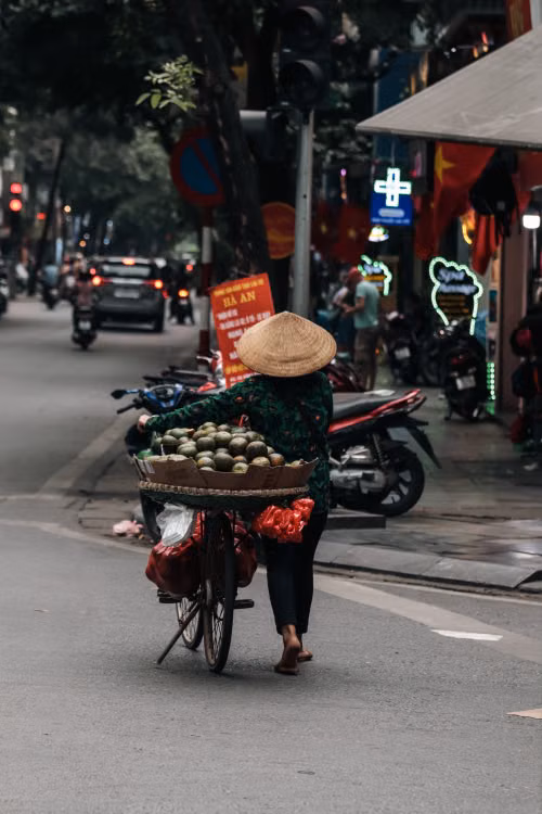 A vendor in a conical hat with a loaded bicycle on a city street