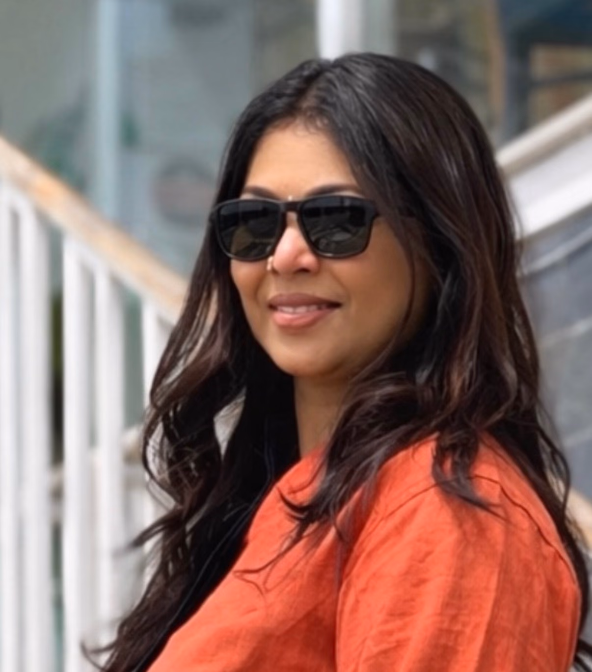 Sreeja Janaki, founder of Le Floral Tours, smiling in sunglasses and a terracotta linen shirt, long dark hair over her shoulder